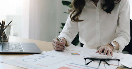 Businesswoman hand holding pen and pointing at financial paperwork with financial network diagram.の写真素材