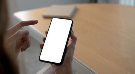 Mockup image blank white screen cell phone.women hand holding texting using mobile on desk at home...