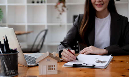 Attractive young female house realtor or real estate agent holding house keys chain and house model....