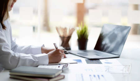 Close up Businesswoman hand holding pen and pointing at financial paperwork, financial charts to...