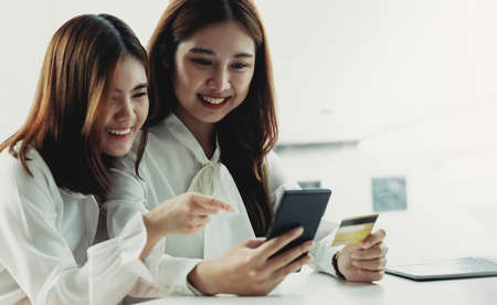 Two young Asian women hold credit cards and happily use their mobile phones for online shopping. business concept and technology digital marketing casual lifestyleの写真素材