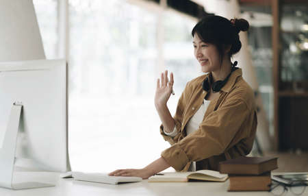 Freelance business women casual wear using laptop working call video conference with customer in workplace in living room at home. Happy young Asian girl relax sitting on desk do job in internet.の写真素材