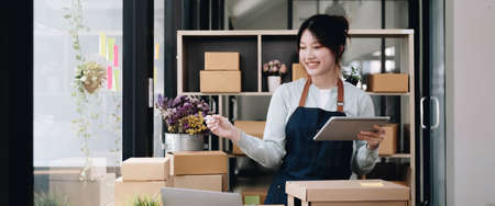 Young beautiful happy asian business woman owner of SME online using laptop receive order from...
