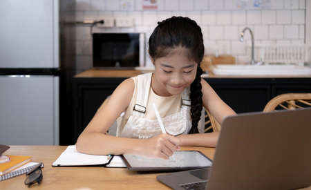 Homeschool Asian little young girl learning online class from school teacher by remote internet meeting application due to coronavirus pandemic. Kid looking computer laptop screen that woman teaching.の写真素材