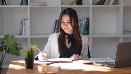 Miniature house in the hands of an Asian woman real estate agent home loan working at the office. Looking at the camera.の写真素材