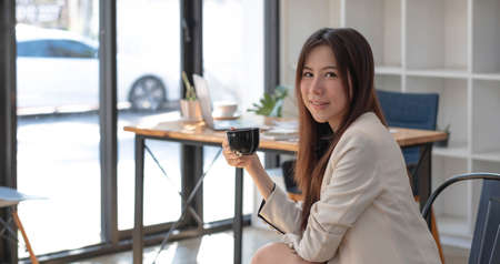 Miniature house in the hands of an Asian woman real estate agent home loan working at the office. Looking at the camera.の写真素材
