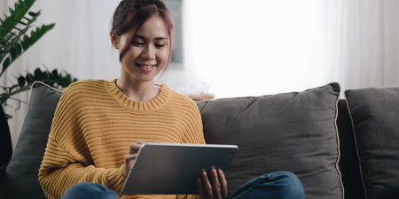 Smiling young woman using laptop, sitting on couch at home, beautiful girl shopping or chatting...