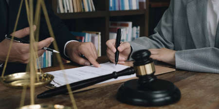 Business woman and lawyers discussing contract papers with brass scale on wooden desk in office....