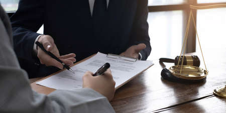 Business woman and lawyers discussing contract papers with brass scale on wooden desk in office....