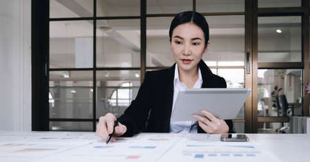 Attractive and charming young Asian businesswoman or financial worker in formal suit using tablet and working with her financial report in the office.の写真素材