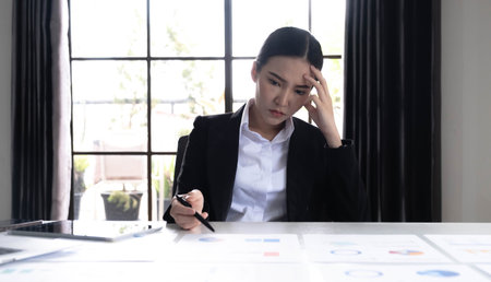 Image of an Asian woman who is tired and overthinking from working with a tablet at the office.