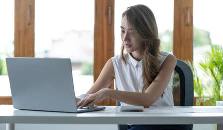 Front view of a beautiful Asian businesswoman working on a tablet coffee cup placed on the office...