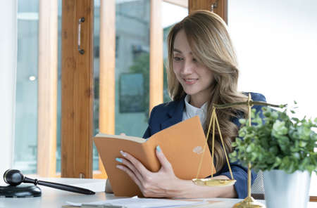 Confident and successful young Asian female lawyer or business legal consultant reading a law book...