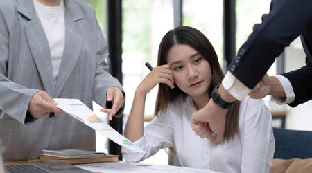 Tired and bored young Asian businesswoman or female office worker getting a complain from her male boss in the office about her work performance.の写真素材