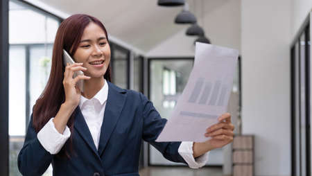 Attractive asian businesswoman or female financial consultant reading a financial report paperwork...