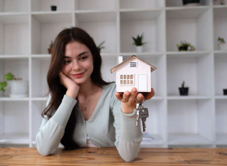 Happy woman hand holding magnifying glass and looking at house model, house selection, real estate concept.の写真素材