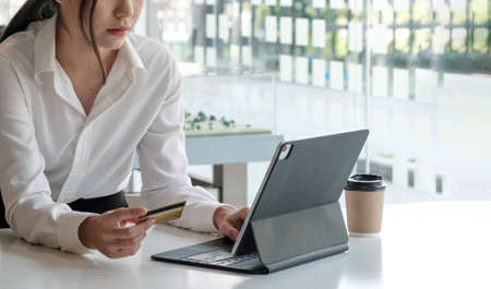 Asian businesswoman working using tablet holding coffee in the office.
