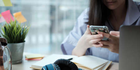 Female student taking notes from a book and using smart phone at home
