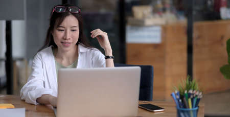 Beautiful young asian woman sitting at coffee shop using laptop. Happy young businesswoman sitting at table in cafe with tab top computer.の写真素材