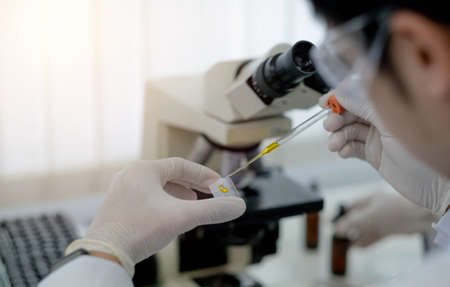 A scientist holding a petri dish in the lab with a monitor and microscope in background.