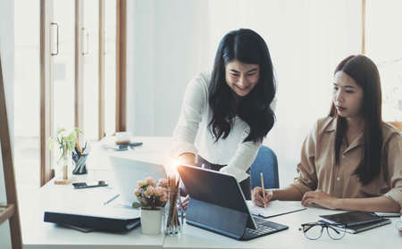 Two young Asian businesswoman discuss investment project working and planning strategy. Business people talking together with laptop computer at office.の写真素材