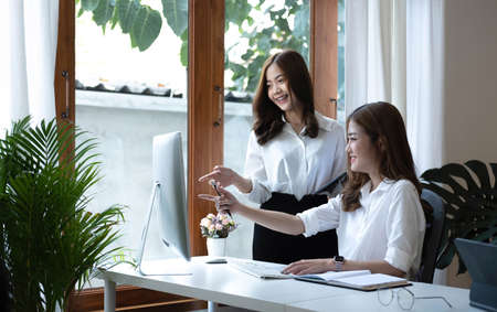 Two young Asian businesswoman discuss investment project working and planning strategy. Business people talking together with laptop computer at office.の写真素材