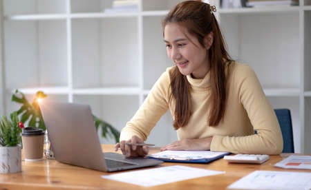 Beautiful Asian businesswoman analyzes charts using laptop calculator at the office.