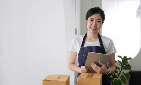 Portrait of Asian young woman SME working with a box at home the workplace.start-up small business owner, small business entrepreneur SME or freelance business online and delivery concept.の写真素材