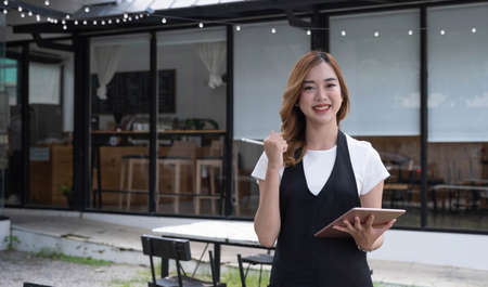 Attractive beautiful young Asian female restaurant or coffee shop waitress noting a customer's order on a digital tablet.の写真素材