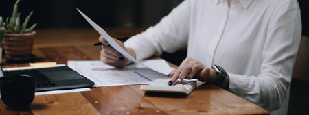 Close-up woman hand press calculator to calculate the company's financial results On the wooden table in the office and business work background, tax, accounting, statistics, and analytical research.の写真素材