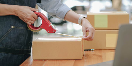 Small business entrepreneur SME, asian young woman,girl owner packing product, checking parcel for delivery to customer, using tape to seal the box, working at home. Merchant online, e commerceの写真素材