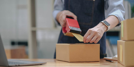 Small business entrepreneur SME, asian young woman,girl owner packing product, checking parcel for delivery to customer, using tape to seal the box, working at home. Merchant online, e commerceの写真素材