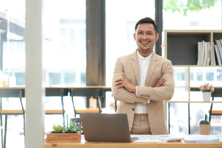 Portrait of a male business owner showing a happy smiling face as he has successfully invested his business using computers and financial budget documents at work.の写真素材