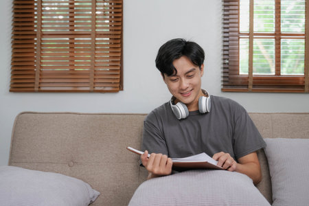 Handsome Asian man using digital tablet while headphones sitting on sofa at home