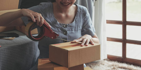 Small business entrepreneur SME, asian young woman,girl owner packing product, checking parcel for delivery to customer, using tape to seal the box, working at home. Merchant online e commerceの写真素材