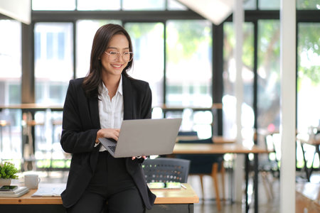 Attractive young brunette asian woman using laptop computer while standing in a officeの写真素材