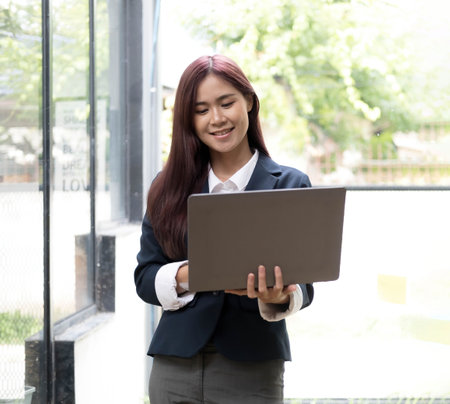 Attractive young asian woman using laptop computer while standing in a office.の写真素材