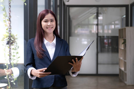 Attractive young asian woman using laptop computer while standing in a office.の写真素材