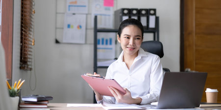 Young woman working on a laptop in the office. Asian businesswoman sitting at her workplace in the office. Beautiful Freelancer Woman working online at her home.の写真素材