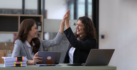 Two young Asian businesswomen show joyful expression of success at work smiling happily with a...