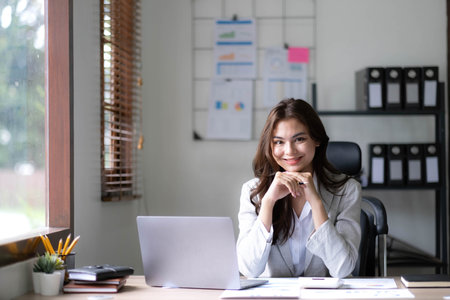 Young woman working on a laptop in the office. Asian businesswoman sitting at her workplace in the office. Beautiful Freelancer Woman working online at her home.