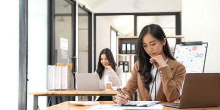 Asian Business woman using calculator and laptop for doing math finance on an office desk, tax, report, accounting, statistics, and analytical research conceptの写真素材