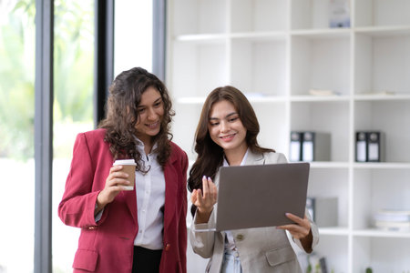 Two beautiful Asian businesswomen standing using digital tablet consulting and analyzing information in office work.の写真素材