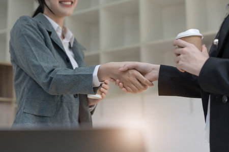 Two Asian businesswomen are shaking hands in the office. business cooperation, business dealing, Congratulations, greeting. close-up hands imageの写真素材