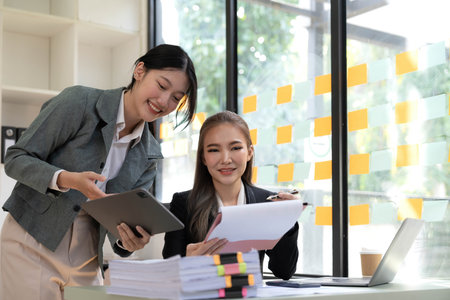 Two young Asian business woman talk, consult, discuss working with new startup project idea presentation analyze plan marketing and investment in the office.の写真素材