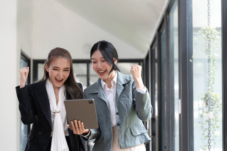 Two beautiful Asian businesswomen standing using digital tablet consulting and analyzing information in office work.の写真素材