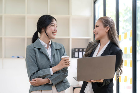 Two beautiful Asian businesswomen standing using digital tablet consulting and analyzing information in office work.の写真素材