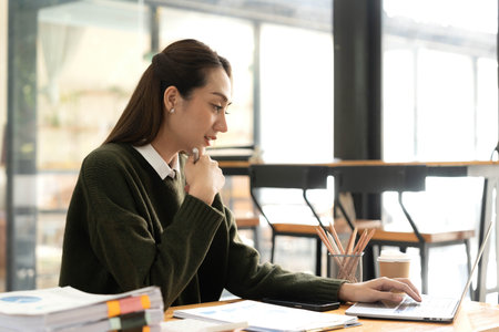 Cheerful business lady working on laptop in office, Asian happy beautiful businesswoman in formal suit work in workplace. Attractive female employee office worker smile.の写真素材