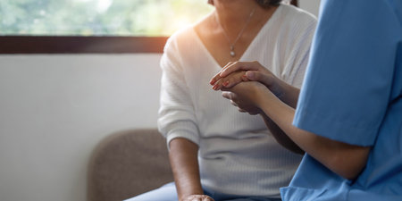 Happy patient is holding caregiver for a hand while spending time together. Elderly woman in nursing home and nurse.の写真素材