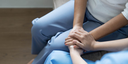Happy patient is holding caregiver for a hand while spending time together. Elderly woman in nursing home and nurse.の写真素材